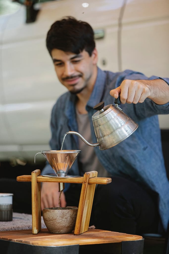 Verkaufstrichter Positive young ethnic guy pouring water into cup while preparing coffee